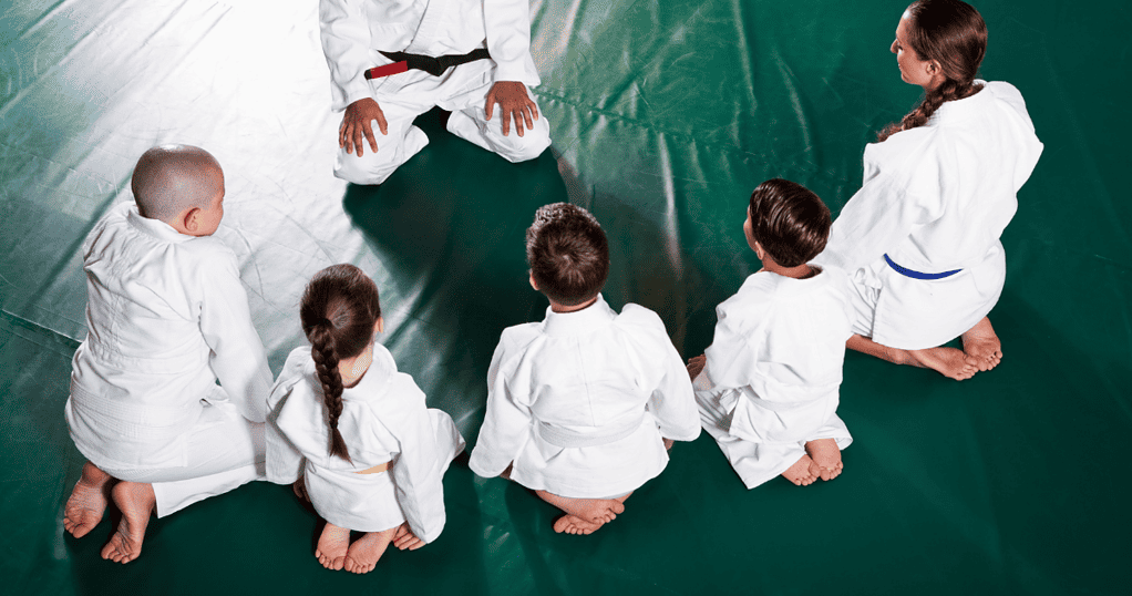 Kids in a BJJ class kneeling as they face their instructor